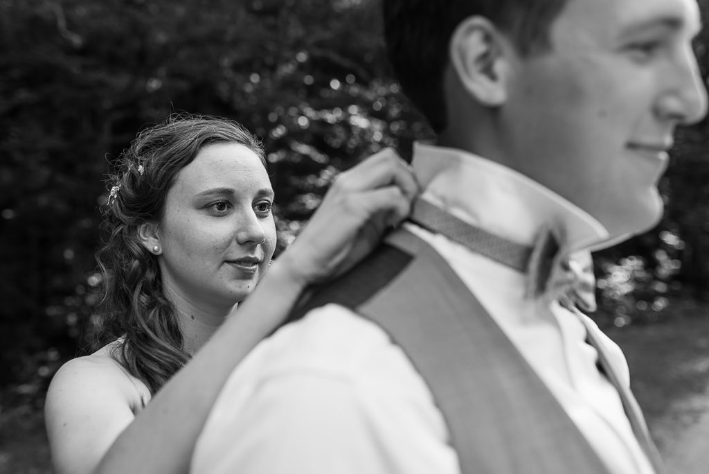 The bride helps her groom get dressed by putting on his bow tie.