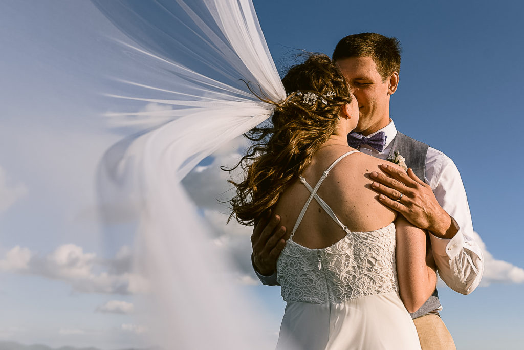Bride and groom hugging while veil flies in the background