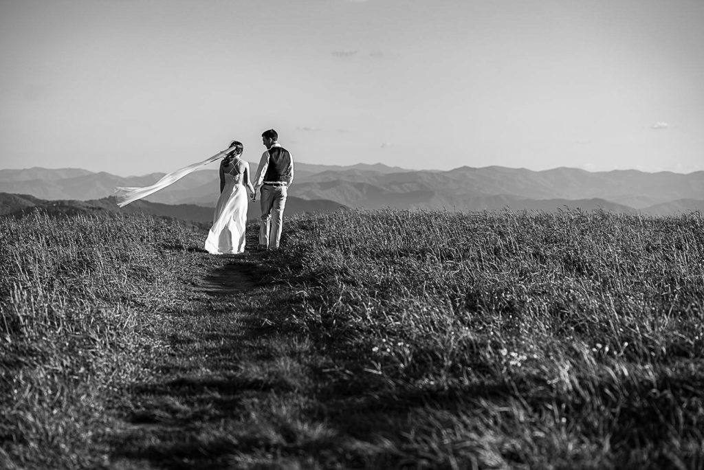 Black and white image of the bride and groom walking hand in hand down the mountain.