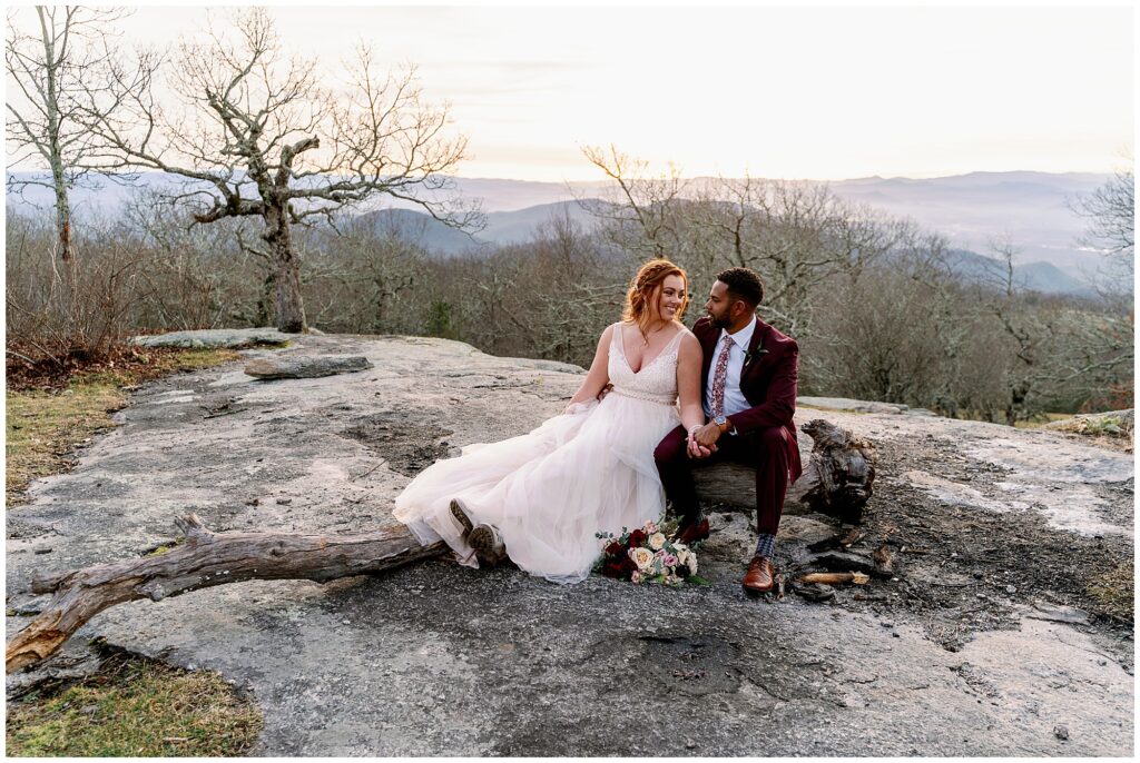 bride and groom sit on a rock and enjoy the mountain top views of bearwallow