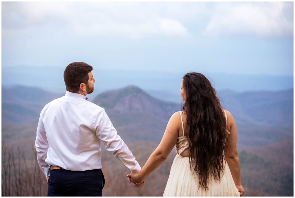 Couples photo of them holding hands looking out at the view of mountains.