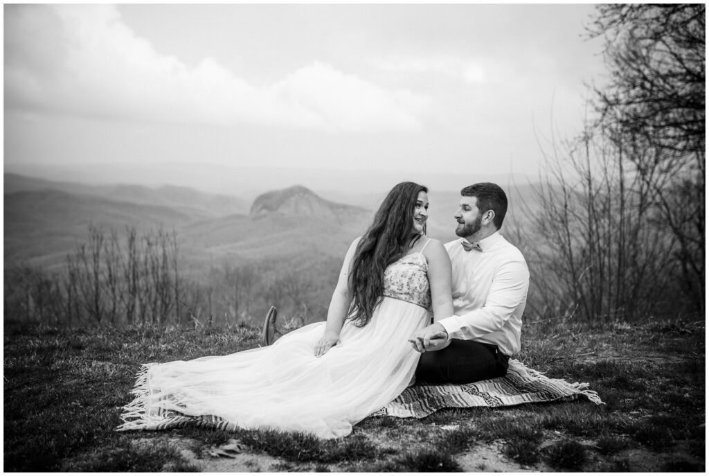 The newlyweds sit on a blanket together on top of the mountain.