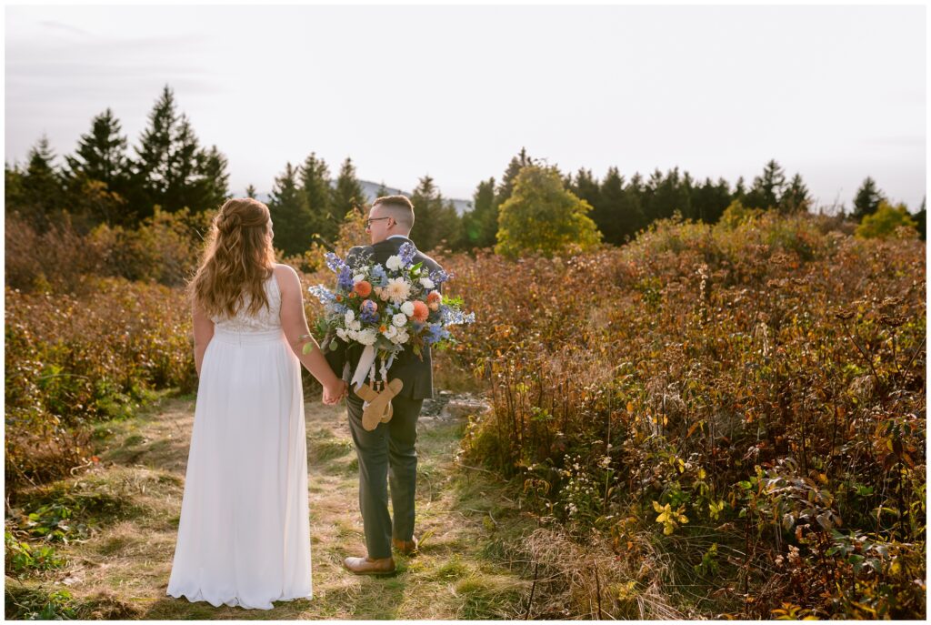 The groom carries the fall bridal bouquet and sandals in a backpack up the mountain.