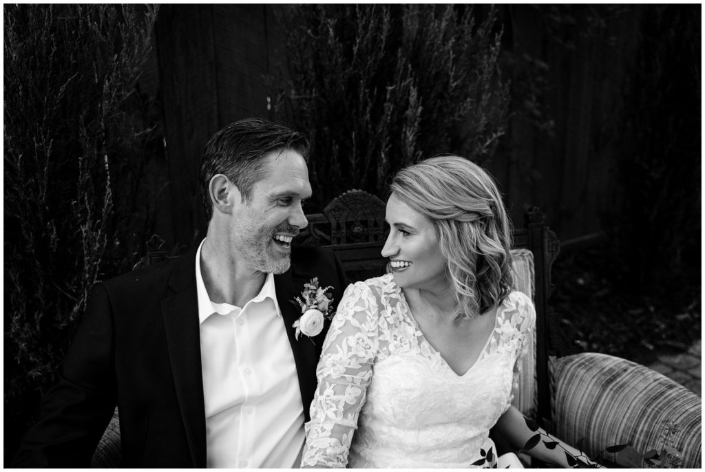 Black and white bride and groom portrait sitting on a bench in a garden.