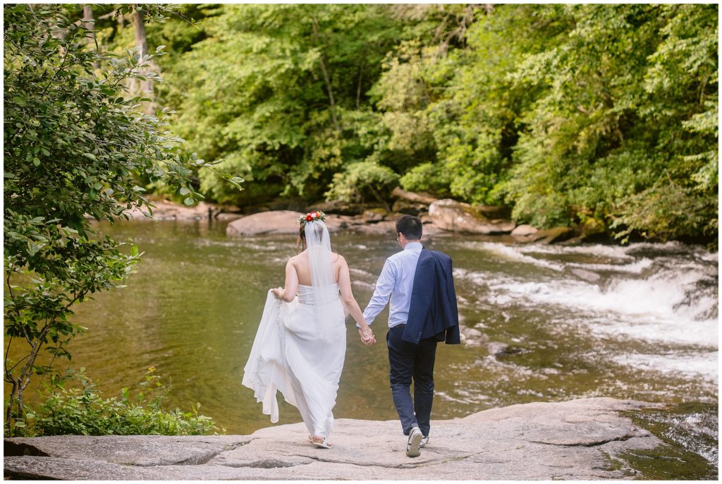 The bride and groom walking hand in hand away from their waterfall elopement in Asheville with Legacy and Legend.