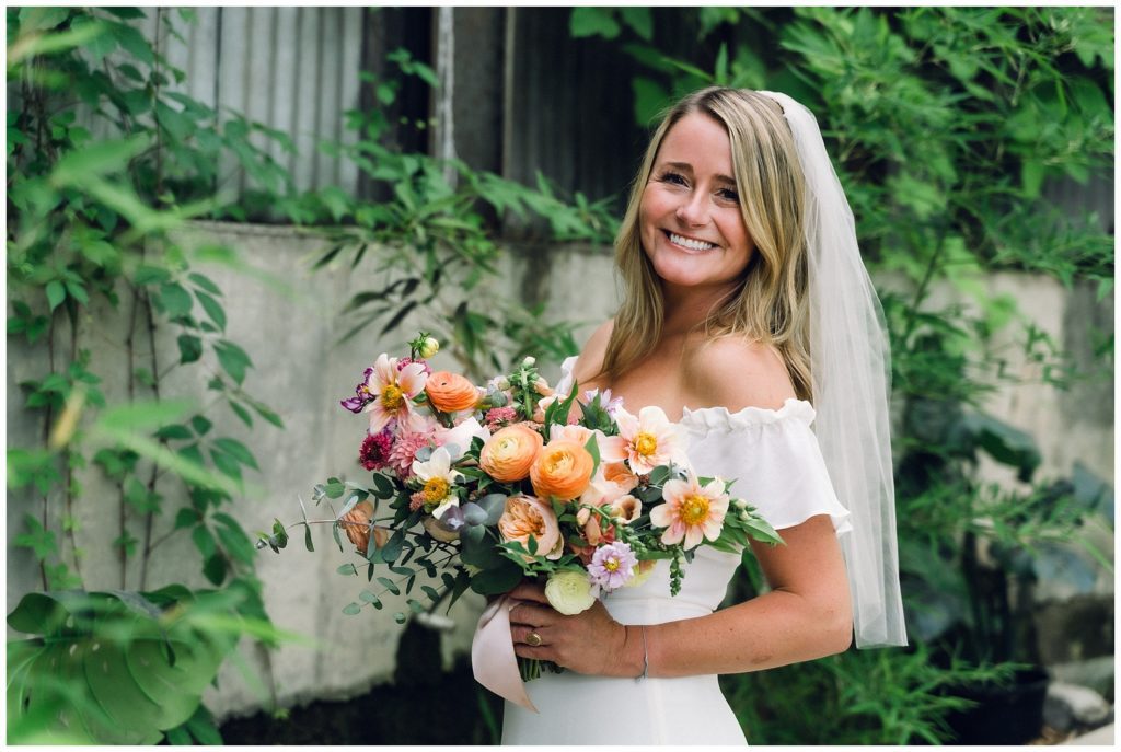 Summer bride showing off her sunset color bridal bouquet with pink and orange flowers.